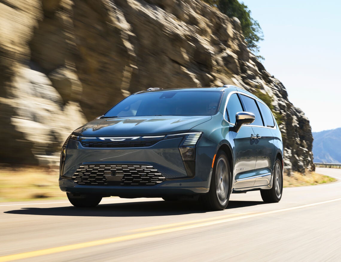 Front three-quarter view of a blue 2027 Chrysler Pacifica Pinnacle driving on a cliffside mountain road.