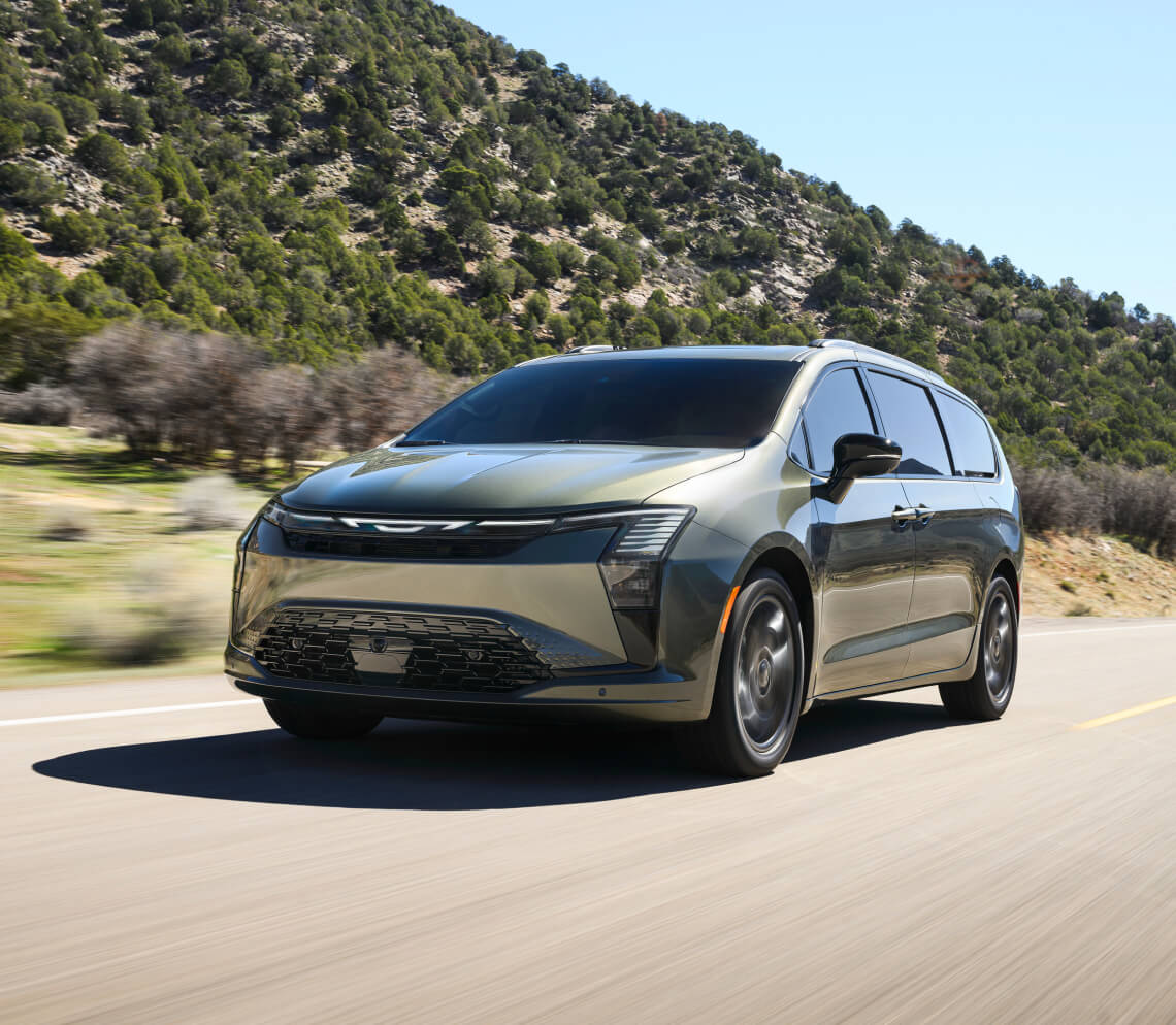 Front three-quarter view of a green 2027 Chrysler Pacifica driving on a mountain road.